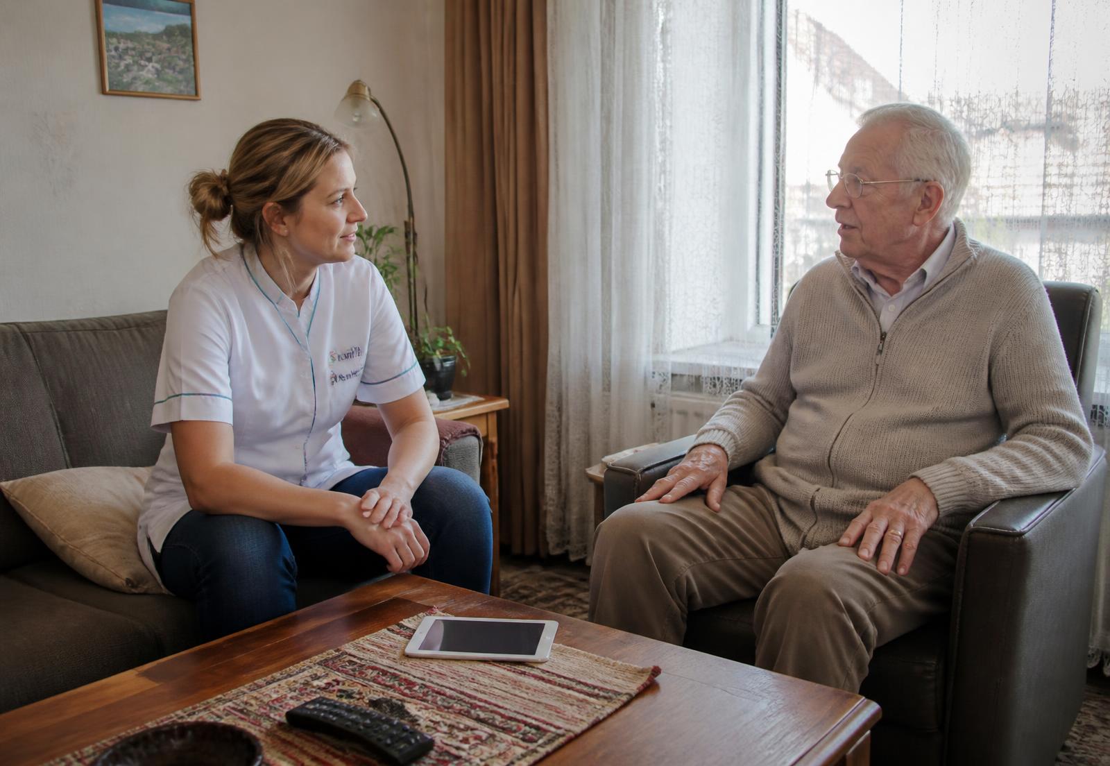 Thuiszorgmedewerker in gesprek met een cliënt in zijn woonkamer